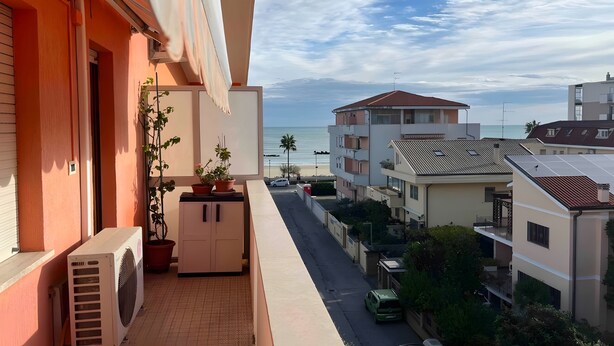 A balcony with potted plants, a white air conditioning unit, and a view of the sea and buildings. - Apartment 'Teresa Al Mare' with Balcony, Wi-Fi and Air Conditioning (Montesilvano)