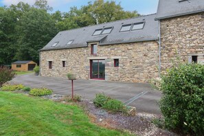 A stone building with a red door, a driveway, and a small garden area.
