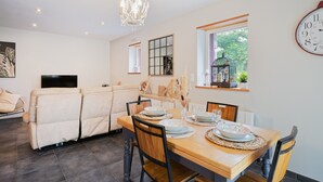 A dining area with a wooden table set for four, a sofa, a TV, and a clock on the wall. - Holiday Home 'La Clémençaie' with Private Terrace, Garden and Wi-Fi (Réminiac)