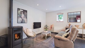 A living room with a fireplace, a sofa, a TV, and a window. - Holiday Home 'La Clémençaie' with Private Terrace, Garden and Wi-Fi (Réminiac)