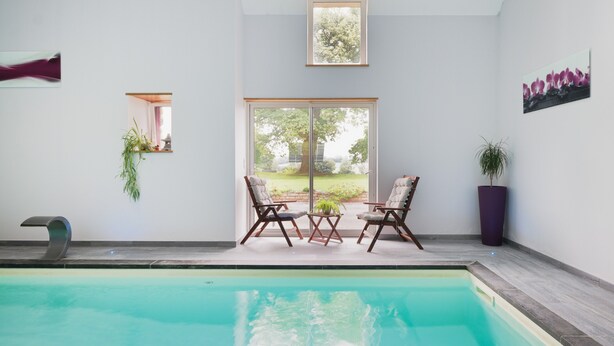 A swimming pool with two chairs and a table, a window with a view of greenery, and a potted plant. - Holiday Home 'La Clémençaie' with Private Terrace, Garden and Wi-Fi (Réminiac)