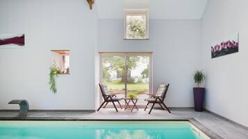 Une piscine avec deux chaises et une table, une fenêtre donnant sur un paysage verdoyant et une plante en pot.