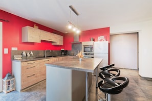 A modern kitchen with a central island, bar stools, and a microwave.