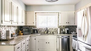 Una cocina con armarios blancos, horno empotrado, lavavajillas y refrigerador de acero inoxidable.