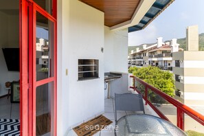 Un balcón con barandilla roja, una pequeña cocina al aire libre y vistas a edificios cercanos.