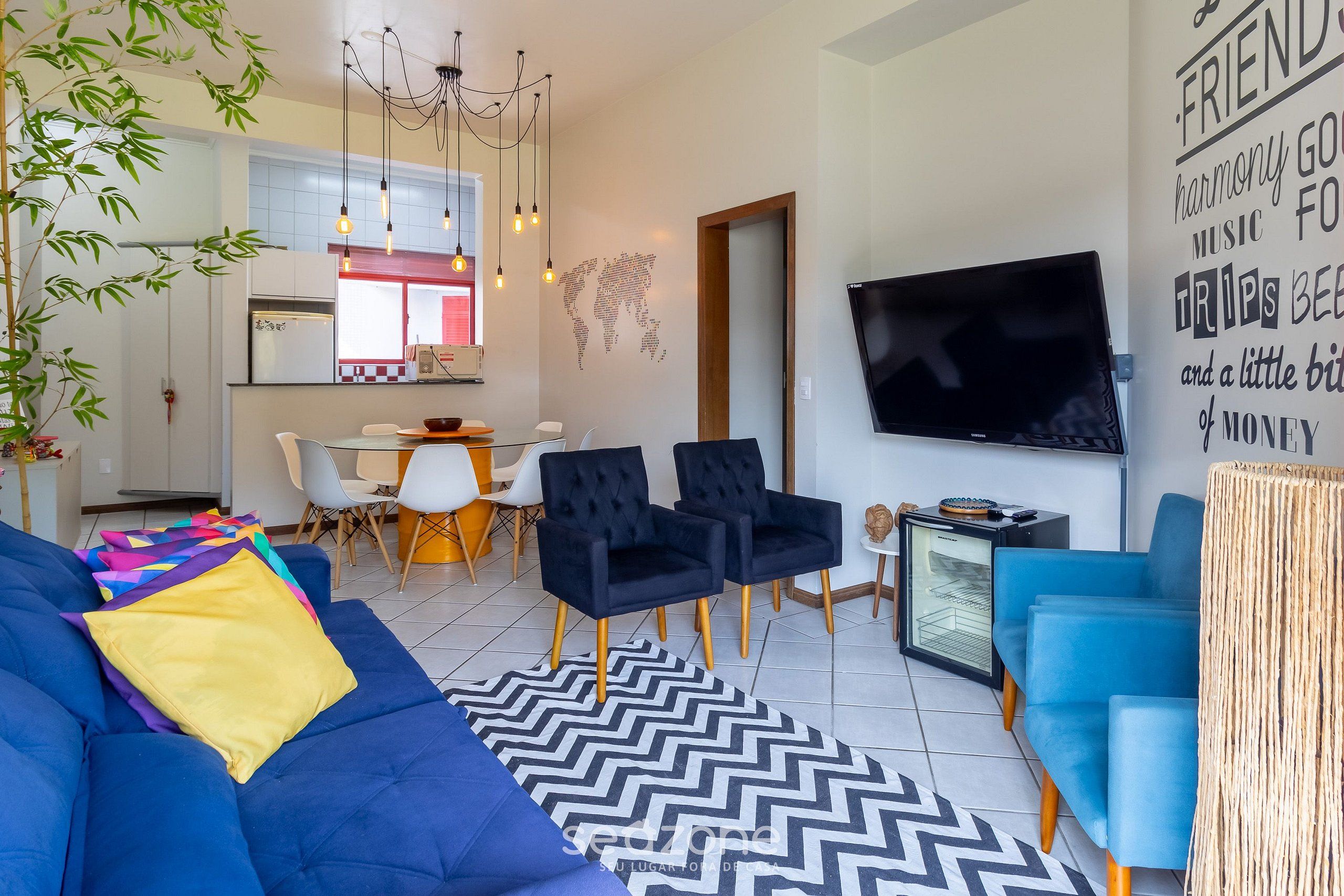 Una sala de estar moderna con un sofá azul, sillas negras, un televisor y una pared con texto motivacional.