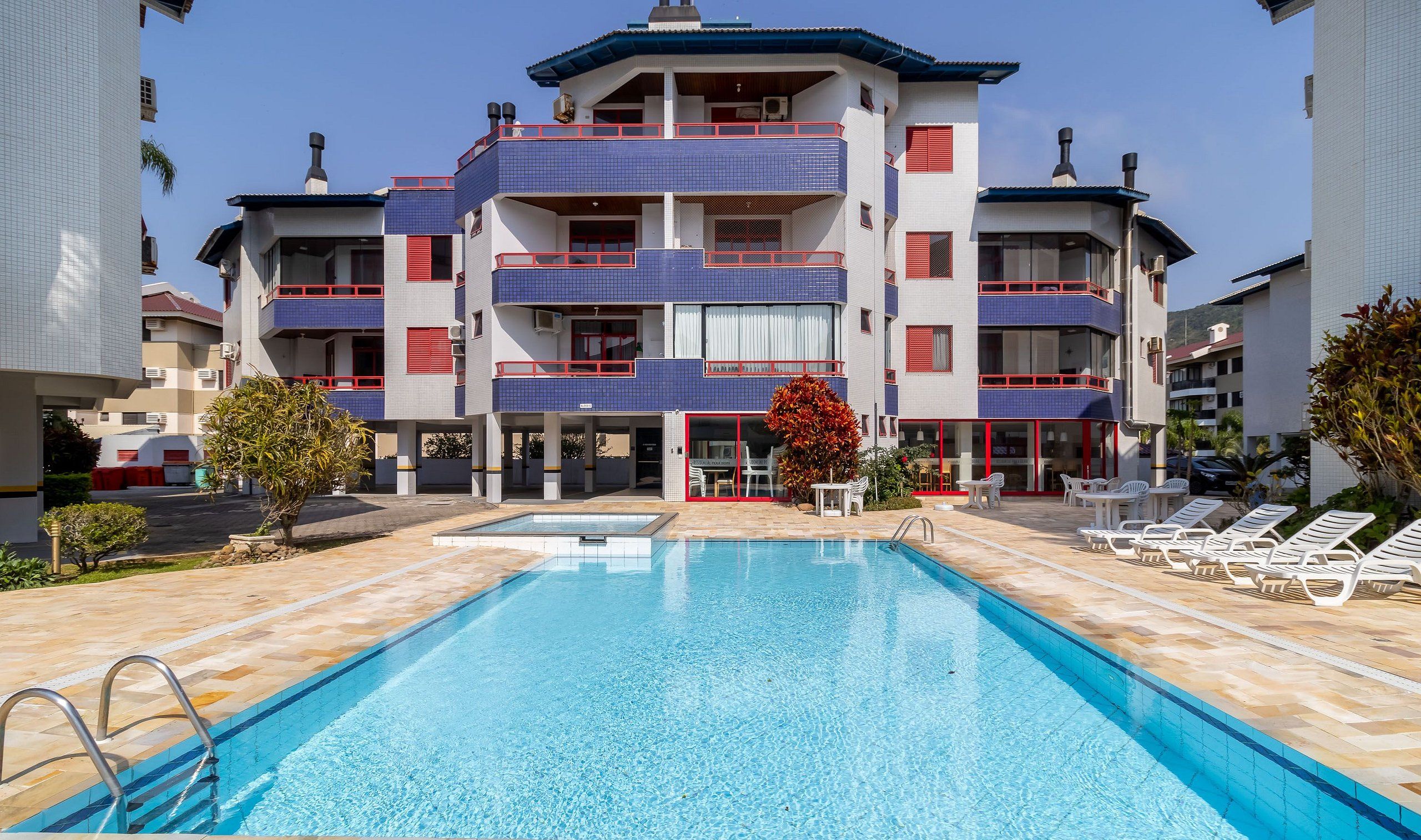 A hotel with a swimming pool, multiple balconies, and a red and blue tiled facade.