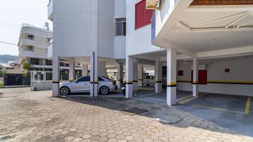 A parking garage with a white tiled exterior, a silver car parked inside, and a covered area with yellow and black striped pillars.
