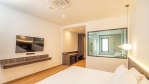 Ett modernt hotellrum med en stor säng, en väggmonterad TV, en inbyggd hylla, en spegel och ett litet pentry.
