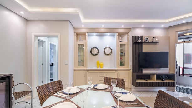 A dining area with a round table set for four, surrounded by wicker chairs. - Apt W/bbq and Access to Praia Brava Rra0103 (Florianópolis)