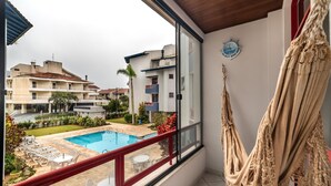 A balcony with a view of a swimming pool, a hammock, and a clock on the wall. - Apt W/bbq and Access to Praia Brava Rra0103 (Florianópolis)