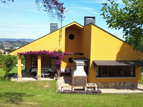 Ein gelbes Haus mit einer Terrasse, Sitzgelegenheiten im Freien und einem Kamin aus Stein.