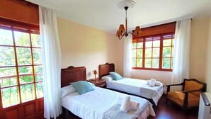 A hotel room with two beds, wooden floors, a chair, and large windows with curtains. - CASONA LA ZAMPUCA (Gijón)