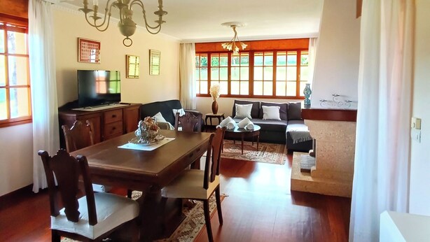 A spacious dining area with a wooden table and chairs, a chandelier, and a view of the garden through large windows. - CASONA LA ZAMPUCA (Gijón)