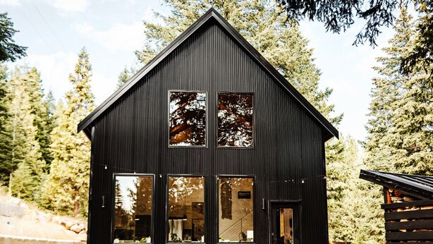 A modern black cabin with large windows and a porch area.