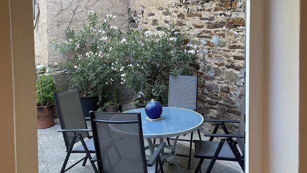 Un espace extérieur aménagé avec une table ronde, quatre chaises et un vase bleu.