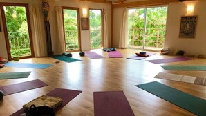 Un estudio de yoga con pisos de madera, ventanas amplias y varias colchonetas y accesorios de yoga.