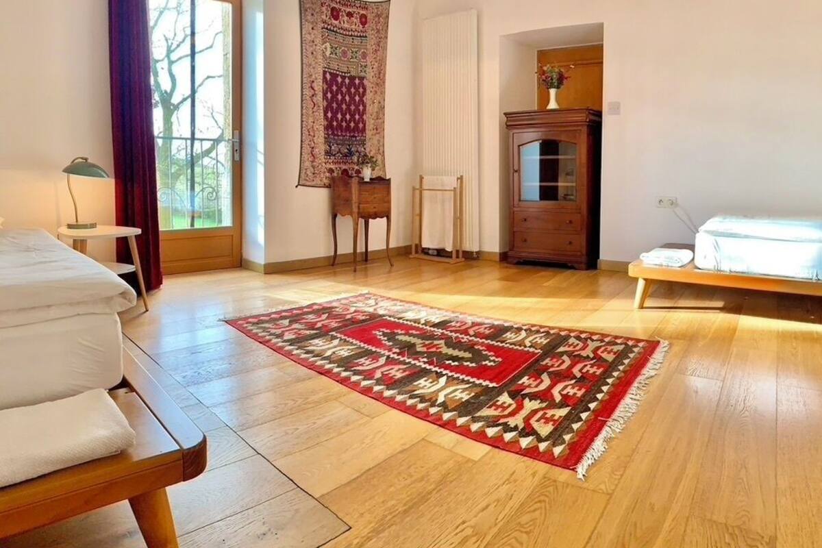 A room with a bed, a wooden floor, a patterned rug, a cabinet, and a window with curtains.