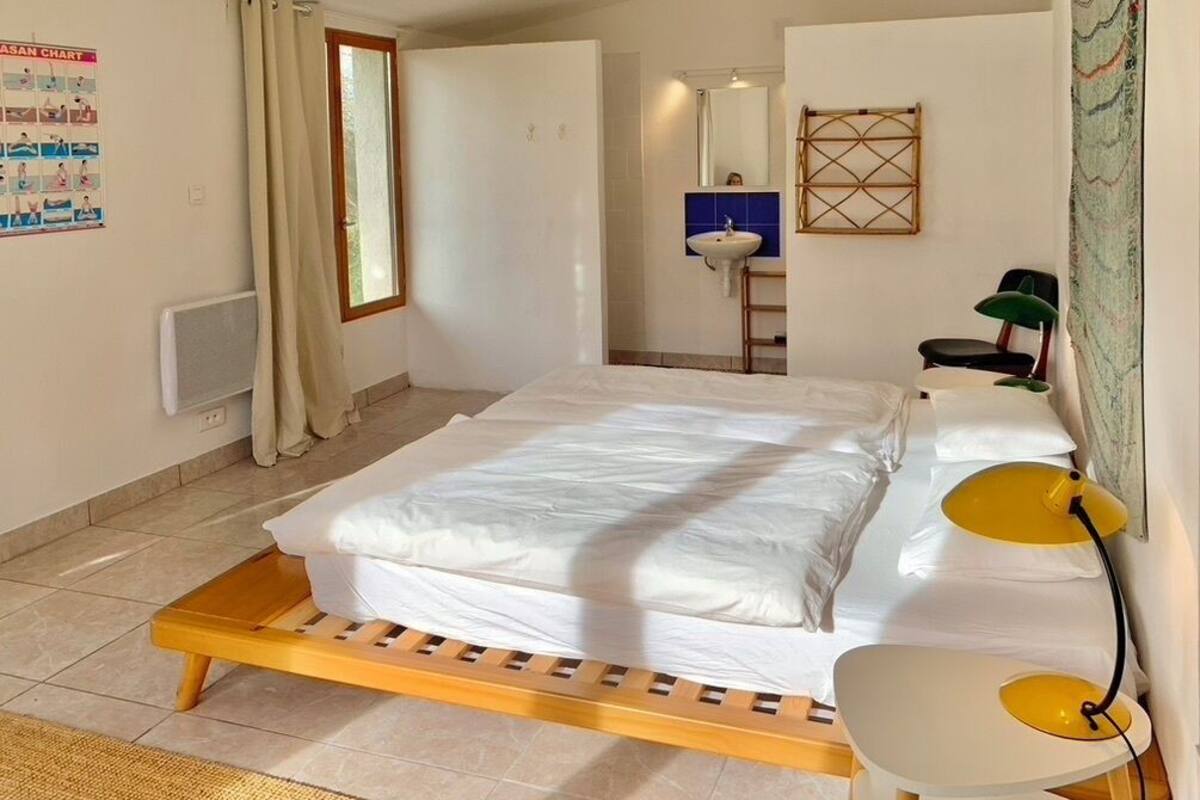 A bedroom with a bed, bedside table, lamp, and a window.