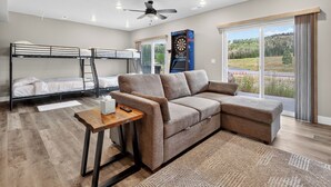 A modern room with a bunk bed, a sectional sofa, a dartboard, and a large window with a view of a green landscape. - Spacious Pet Friendly Mountain Townhome | Game Room + Near Slopes (Brian Head)