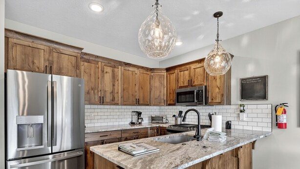 A modern kitchen with wooden cabinets, stainless steel appliances, a marble island, and pendant lighting. - Spacious Pet Friendly Mountain Townhome | Game Room + Near Slopes (Brian Head)