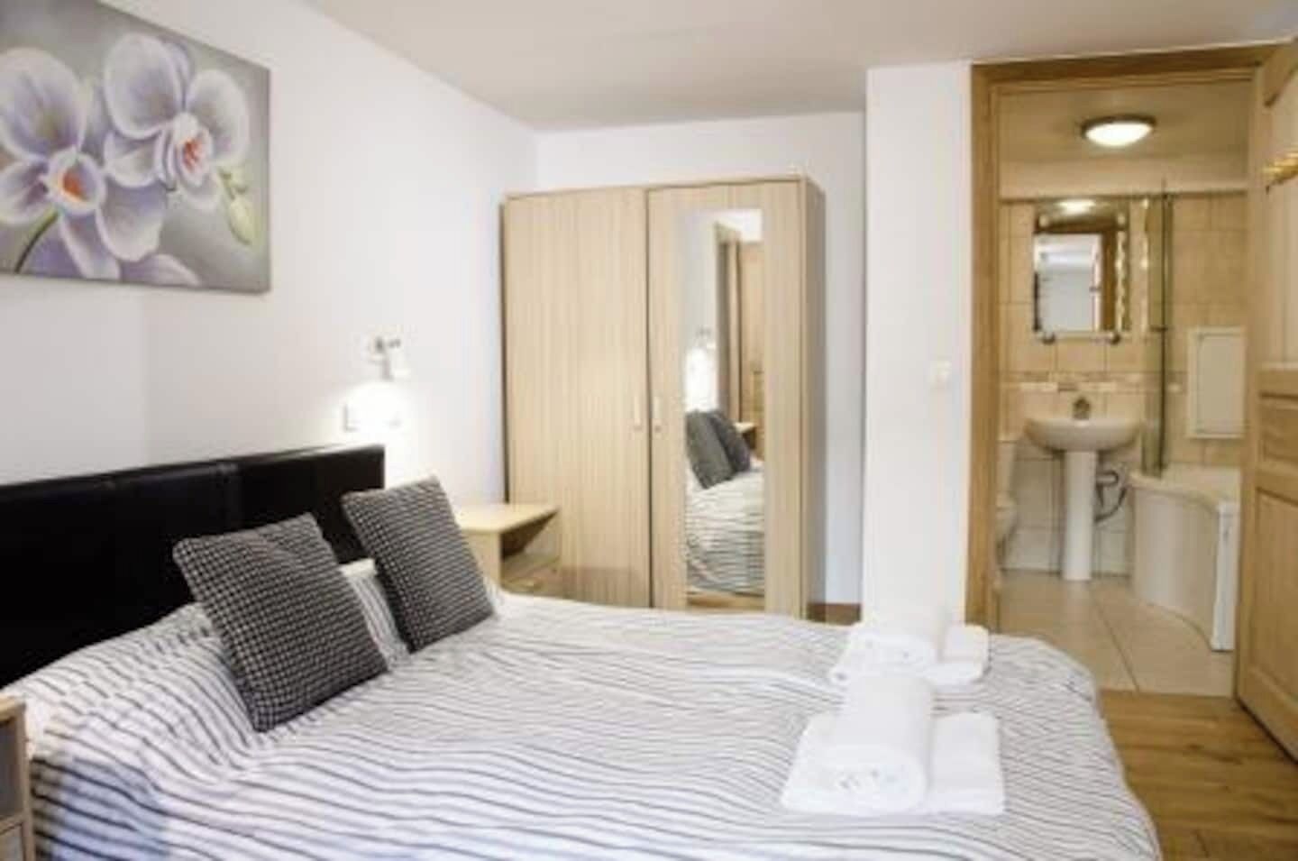 Ein Hotelzimmer mit Bett, Nachttisch, Spiegel, Kleiderschrank und einem durch eine offene Tür einsehbaren Badezimmer.