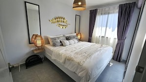 A bedroom with a large bed, two bedside lamps, a mirror, and a decorative leaf wall art piece. - C212 NOON Village (Chalong)