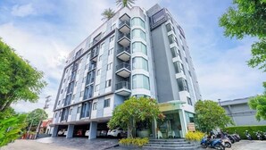 A multi-story hotel with a modern design, featuring balconies, a covered entrance, and a parking area with motorcycles. - C212 NOON Village (Chalong)