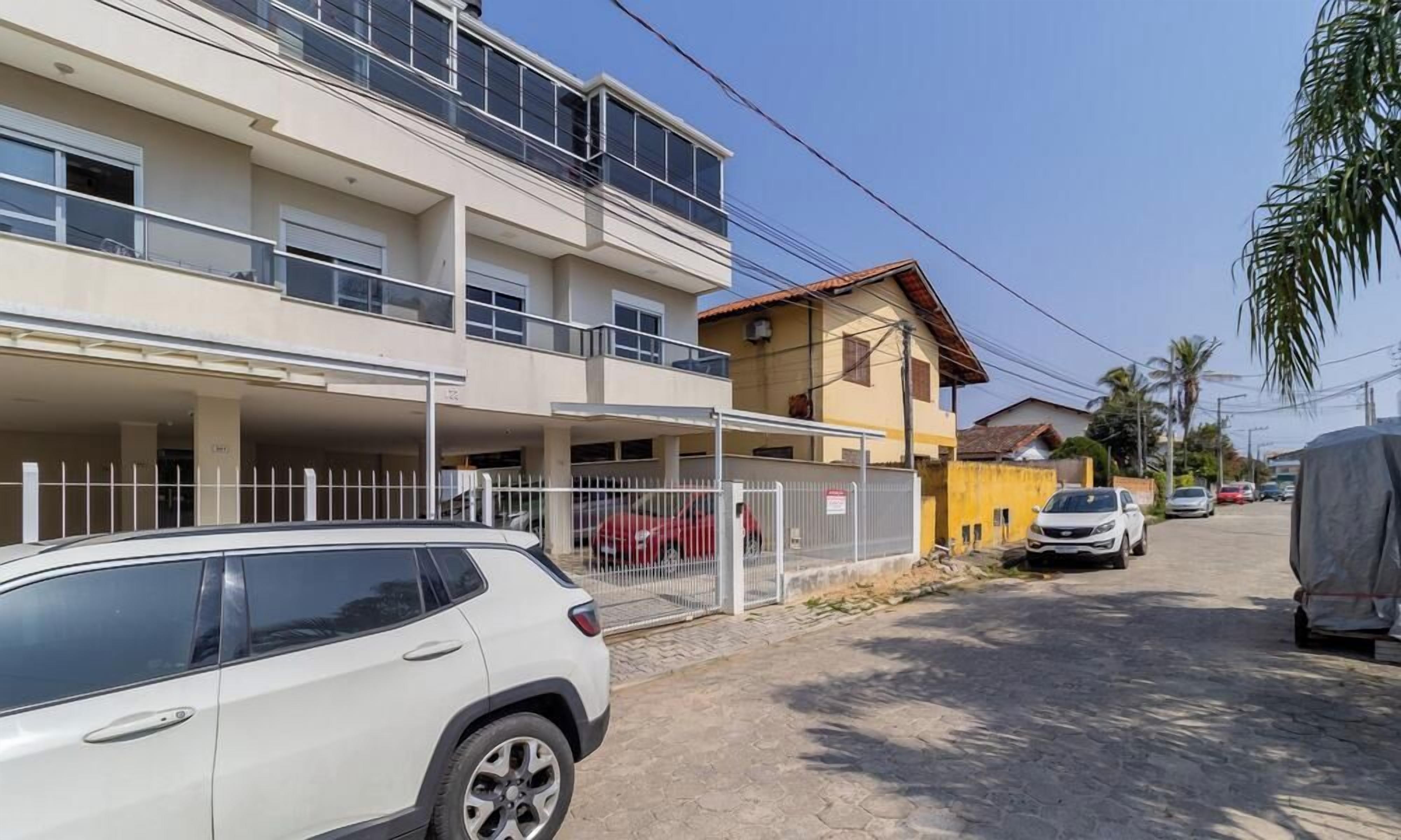 A multi-story residential building with a covered parking area, a fenced section, and a street view with parked cars.