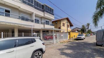 A multi-story residential building with a covered parking area, a fenced section, and a street view with parked cars.