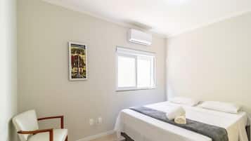 A hotel room with a bed, a chair, a window, and an air conditioning unit.