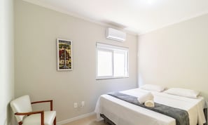 A hotel room with a bed, a chair, a window, and an air conditioning unit.