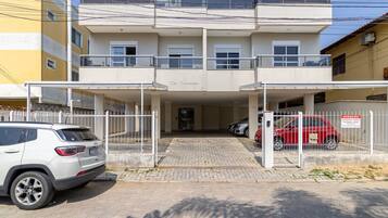 Un edificio de varios pisos con entrada protegida por un portón, zona de estacionamiento techada y un automóvil visible al frente.