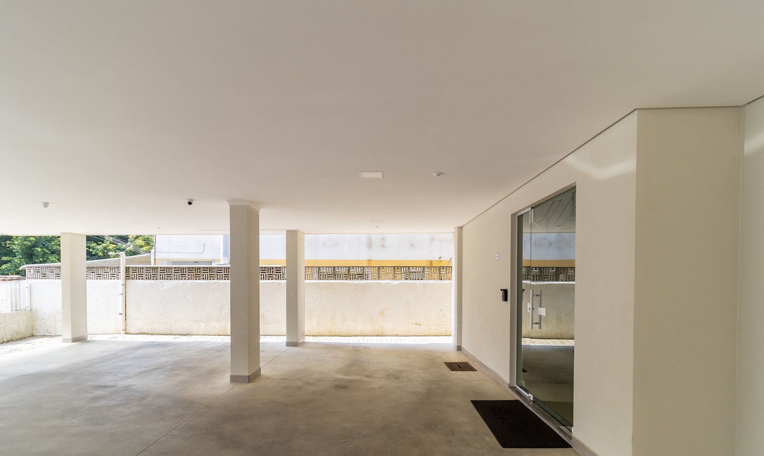 A spacious indoor area with a concrete floor, white walls, and a glass door leading to an outdoor balcony.