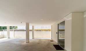 A spacious indoor area with a concrete floor, white walls, and a glass door leading to an outdoor balcony.