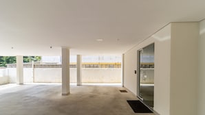 Et rummeligt indendørs område med betongulv, hvide vægge og en glasdør, der fører til en udendørs altan.