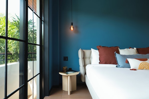 A modern bedroom with a large bed, a bedside table, a hanging light, and a view of greenery outside.