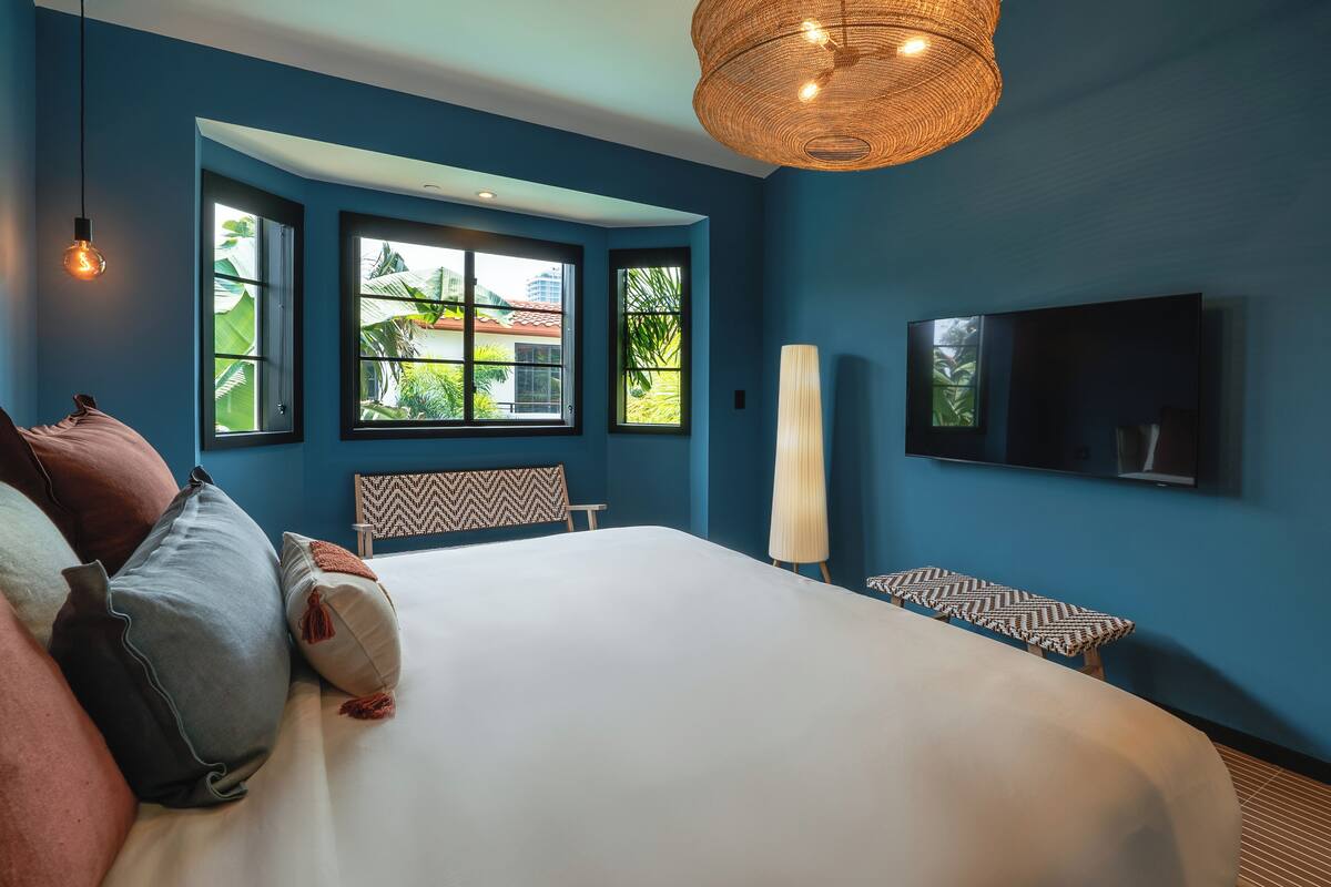 A bedroom with a large bed, a television, and a window with a view of greenery.