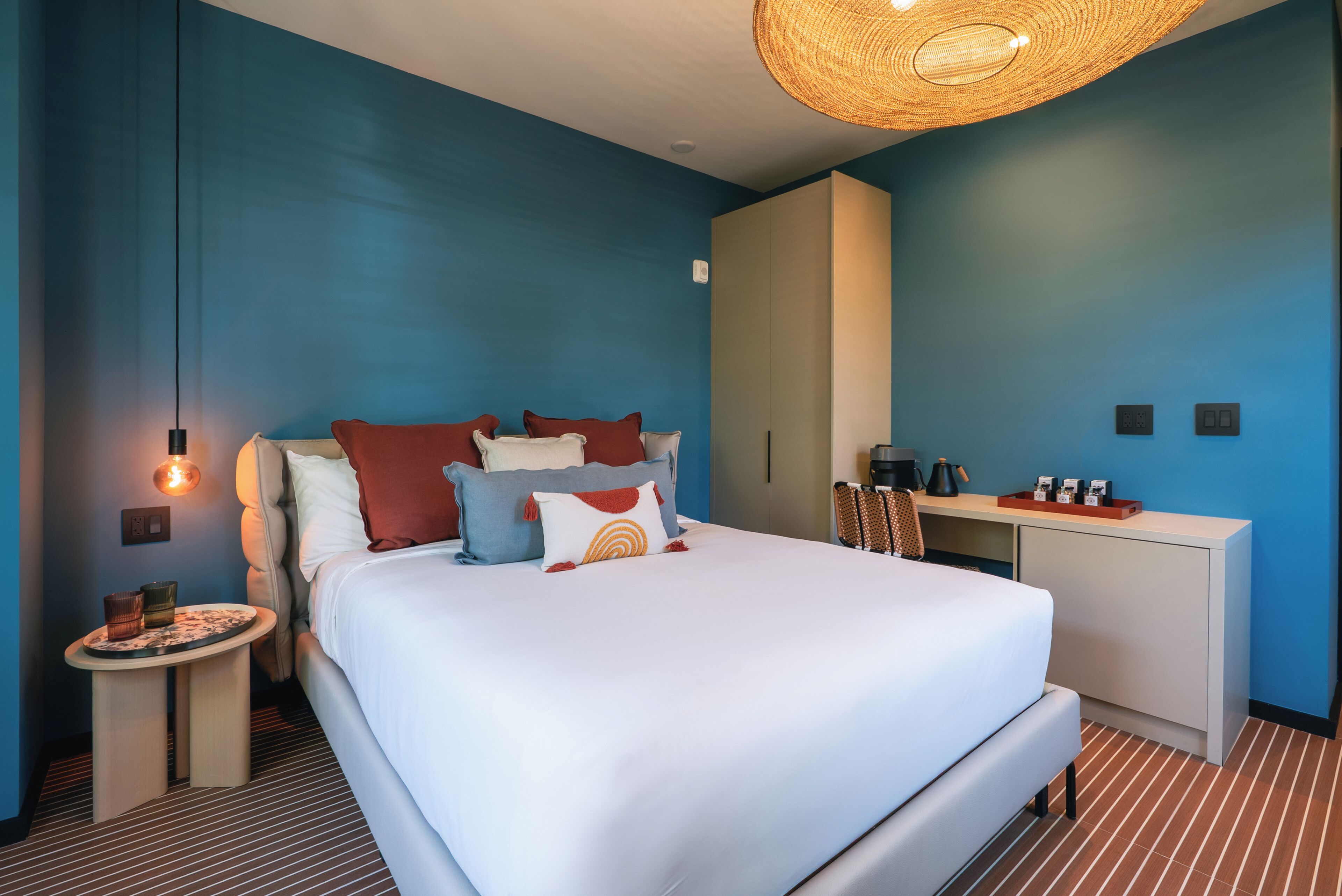 A modern hotel room with a large bed, a bedside table, a wardrobe, and a hanging light fixture.