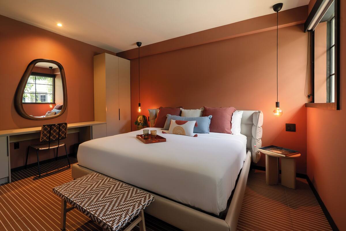 A hotel room with a large bed, a desk, a chair, a small table, and a mirror on the wall.