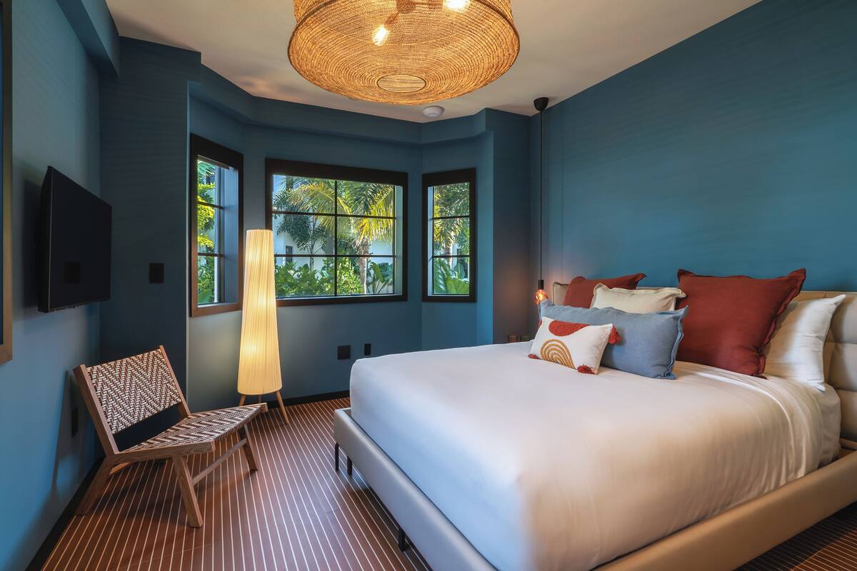 A bedroom with a large bed, a chair, a lamp, and windows with a view of trees.