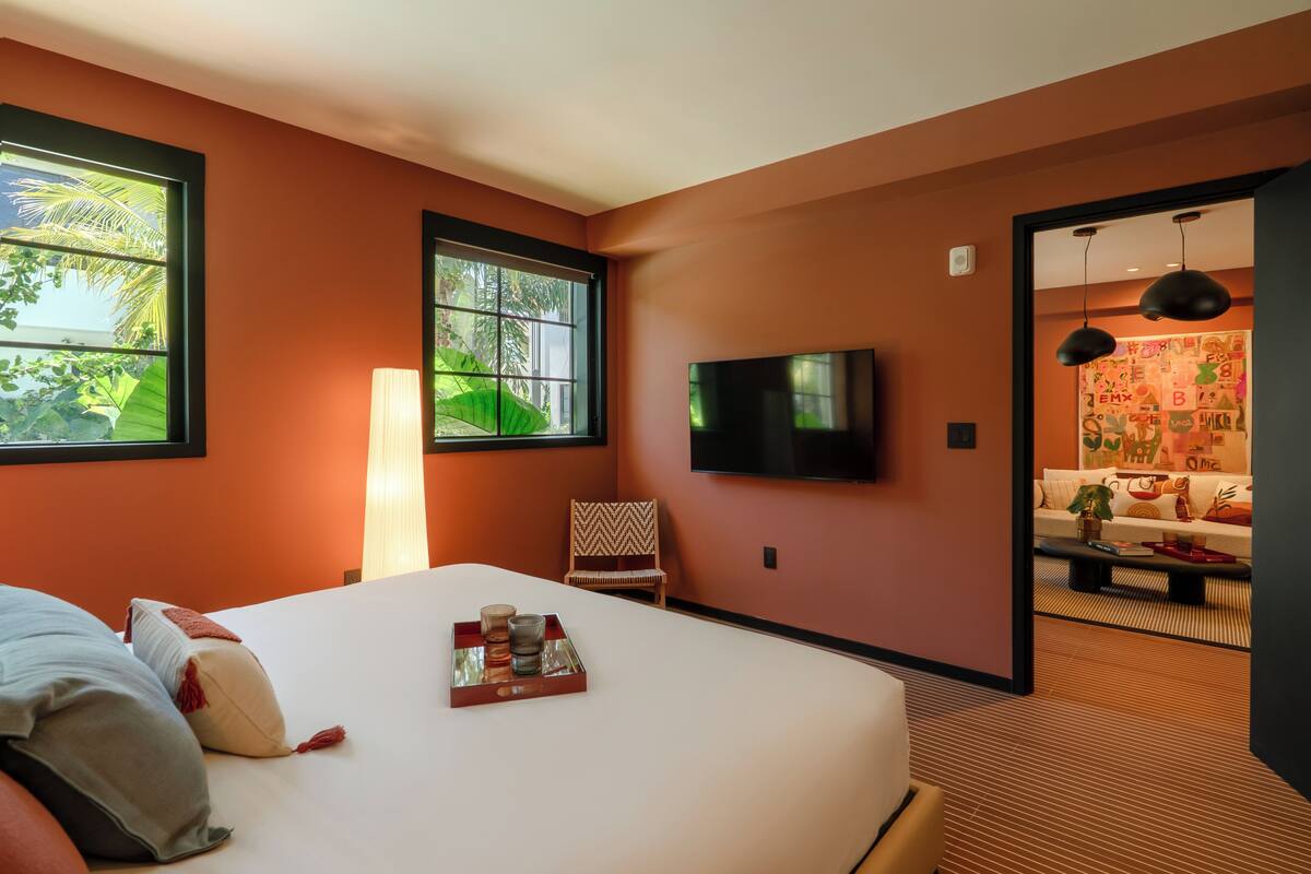 A hotel room with a large bed, a TV mounted on the wall, and a view of the outdoors through a window.