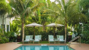 A swimming pool with lounge chairs and umbrellas, surrounded by lush greenery and palm trees.