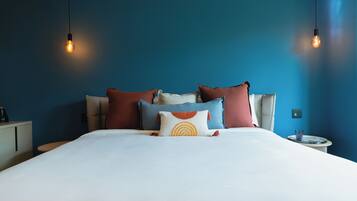 A neatly made bed with multiple pillows, a bedside table with a glass, and two hanging light bulbs.