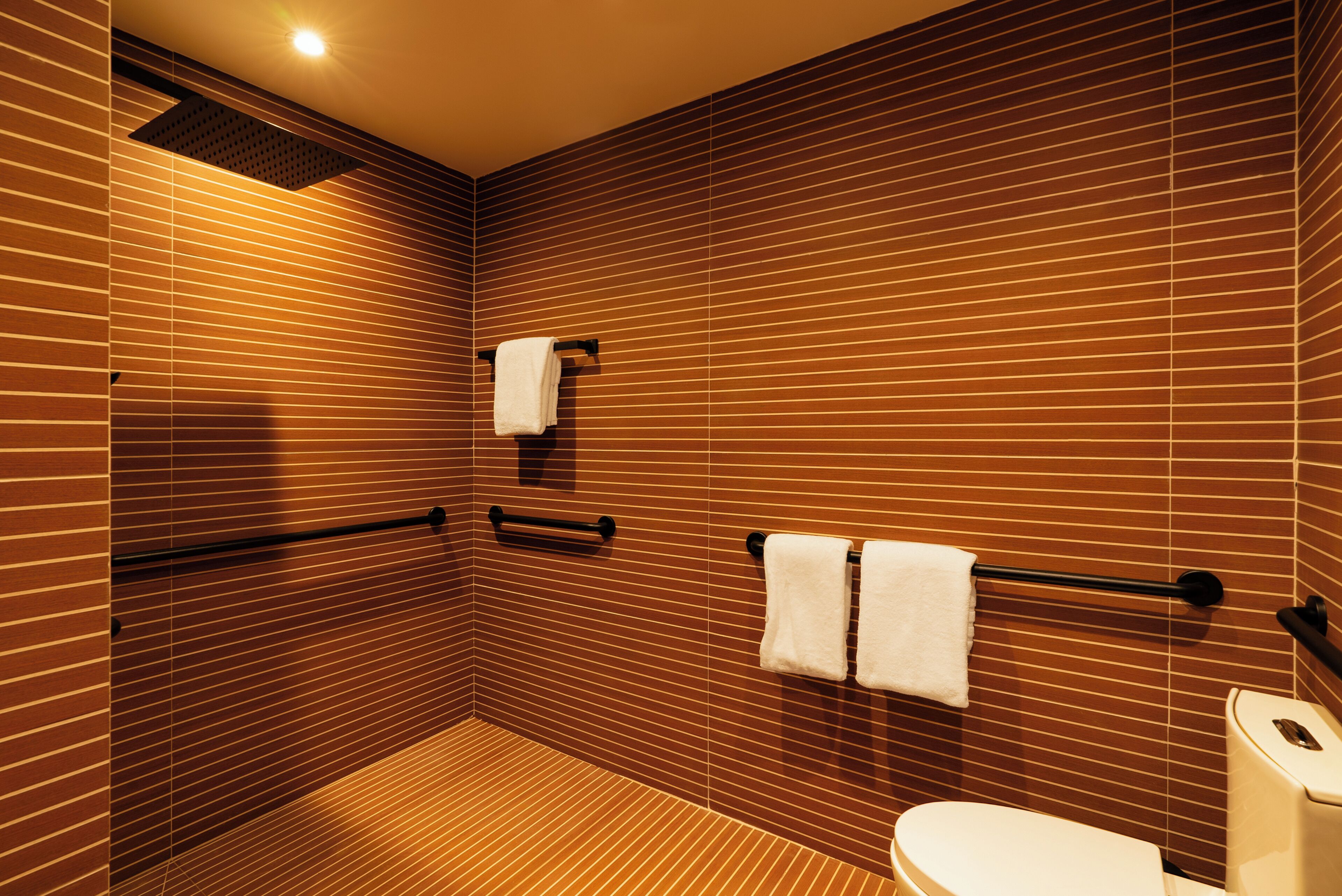 Baño con pared de listones de madera, inodoro y dos toalleros con toallas.