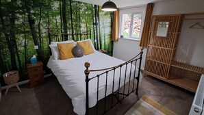 A bedroom with a bed, a hanging light, a window, a wardrobe, and a wall with a forest mural. - Robin's Nest, your home from home (Wilbarston)