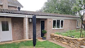 A brick house with a tiled roof, a front door, and a small garden with a stone wall and plants. - Robin's Nest, your home from home (Wilbarston)