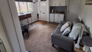 A compact living space with a kitchenette, a dining area, and a seating area with a sofa and a fan. - Robin's Nest, your home from home (Wilbarston)