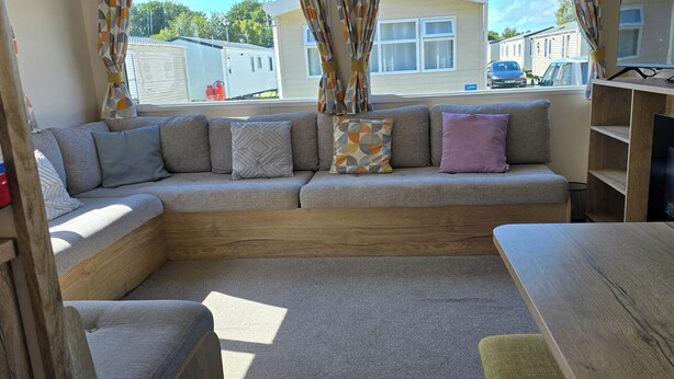 A cozy RV interior with a sectional sofa, a wooden table, and a TV on a stand.