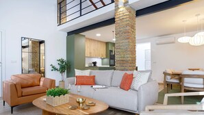 Una sala de estar moderna con un sofá, una mesa de centro y sillas. Se ve una cocina al fondo.